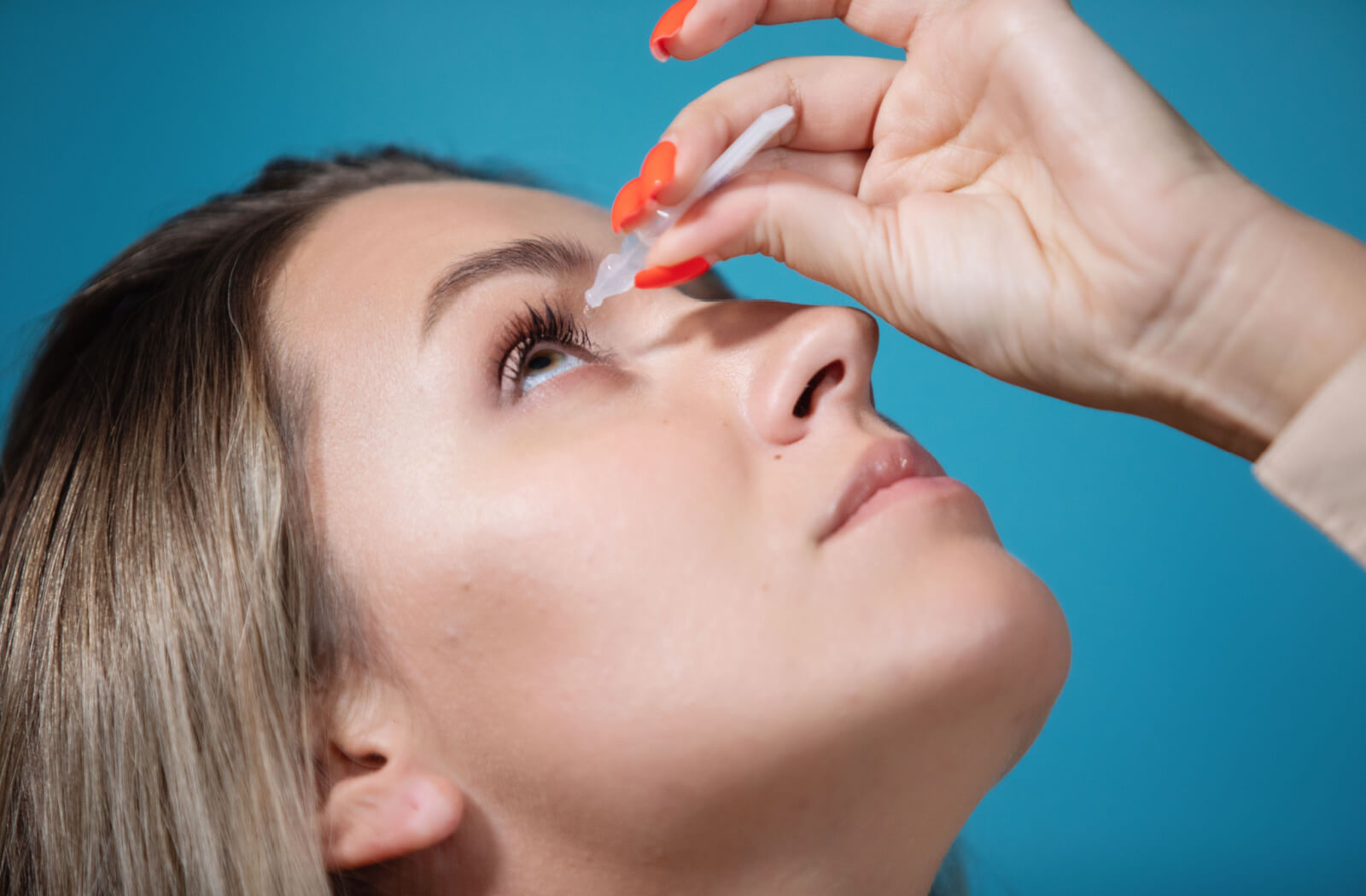 A lady is putting drops of Atropine in her right eye to help treat lazy eye