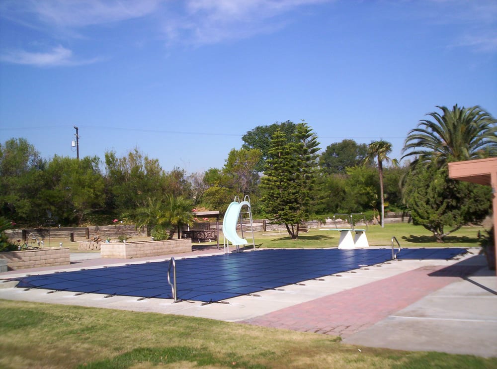 Blue mesh pool cover installed on a rectangular swimming pool with a slide