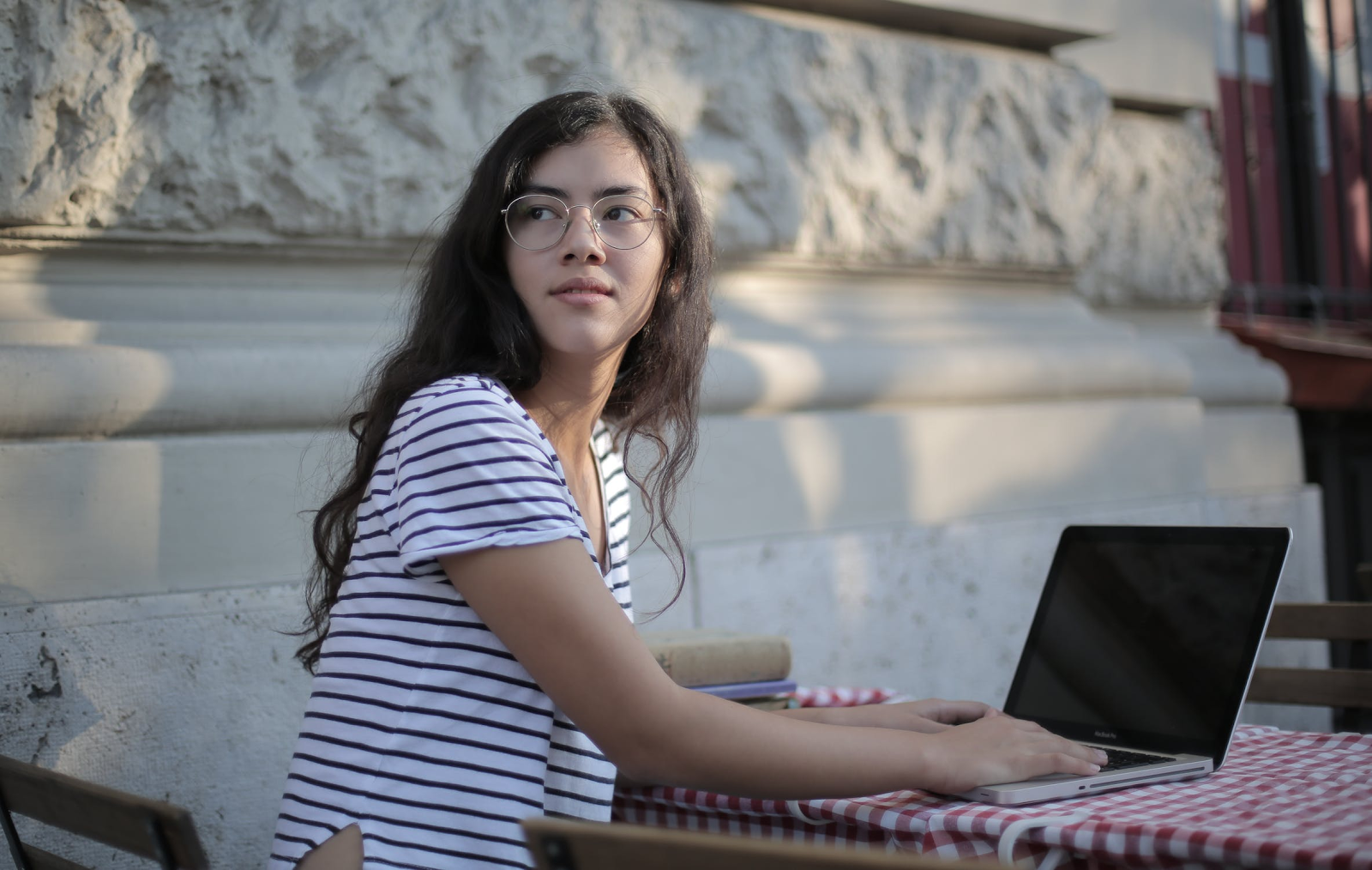 Woman in a striped t-shirt sitting at an outside table with her laptop, looking behind her