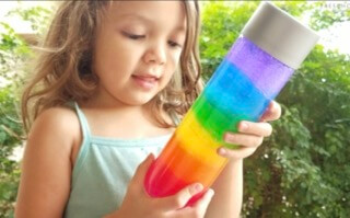 A child holding a rainbow sensory bottle