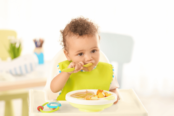 young child sitting in a high chair eating pureed fruit