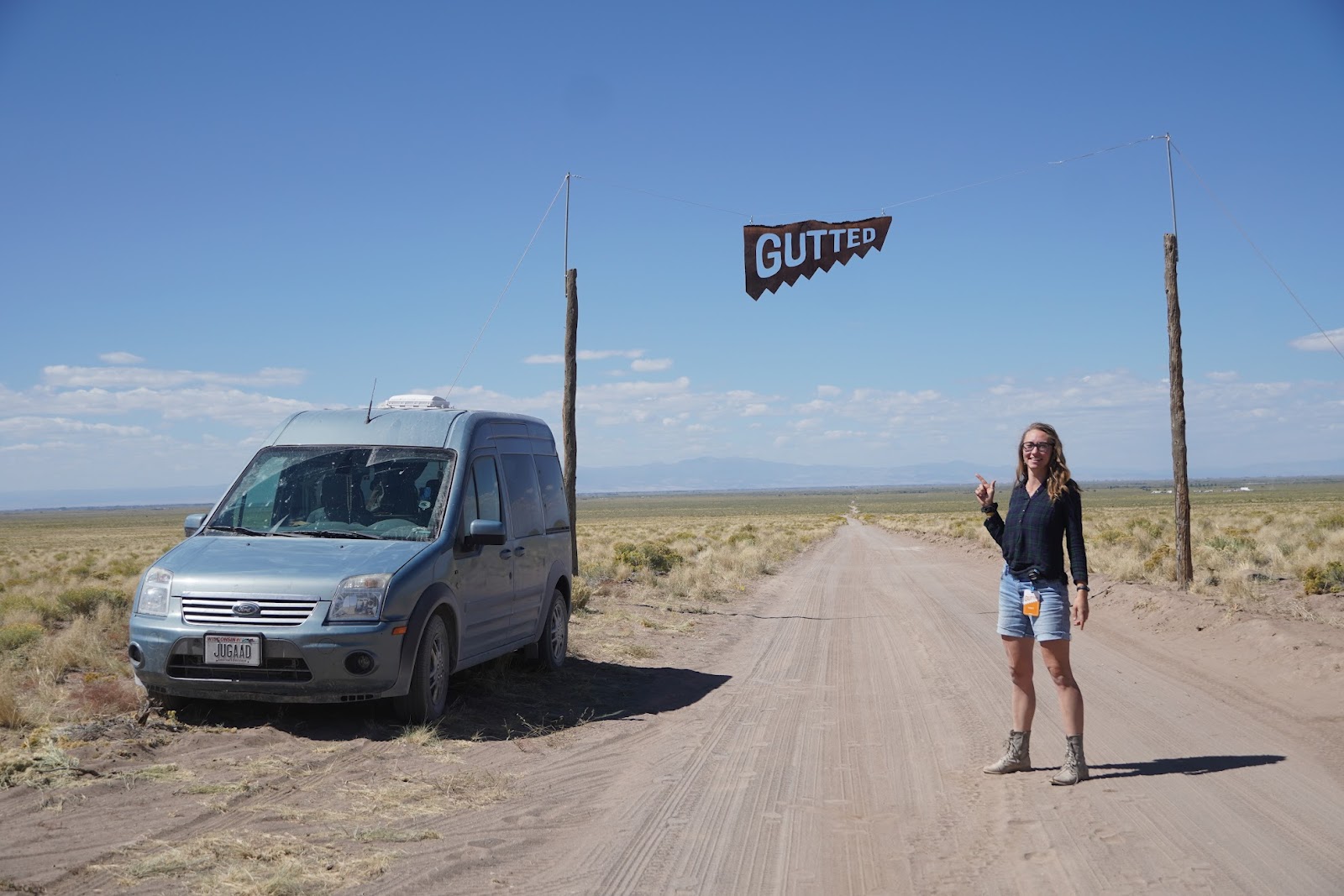 Huemer stands on a dirt road, smiling and pointing to the van beside her