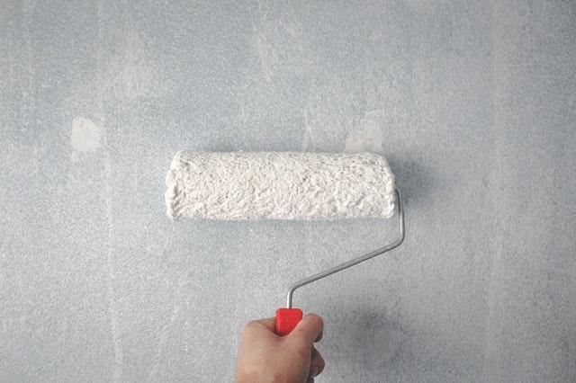  A person painting a wall white, symbolizing questions to ask your clients before starting a painting project
