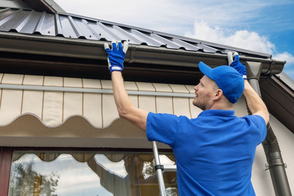 A man in blue installing eavestrough on a home.