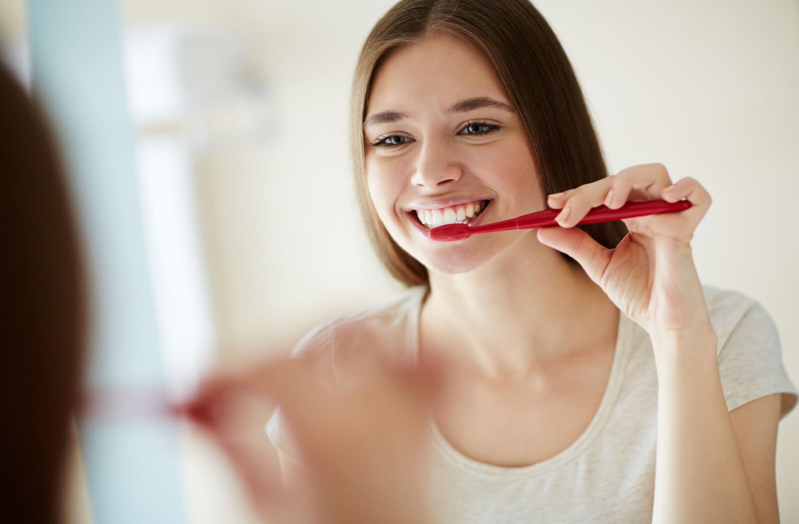 A young woman standing in front of a mirror brushing her teeth with a toothbrush.