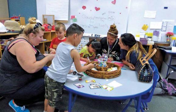 Un grupo de niños y tres cuidadores sentados alrededor de una mesa haciendo manualidades.