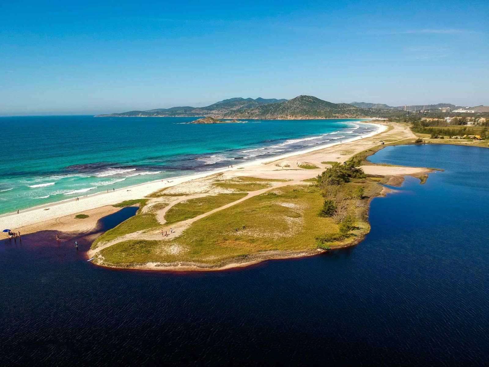 Vista aérea da Lagoa e Praia do Foguete. Uma de frente para a outra, separadas por uma extensa orla, faixa de areia e gramado. Lagoa em tom azul escuro, em contraste com o azul claro, cristalino, do mar.