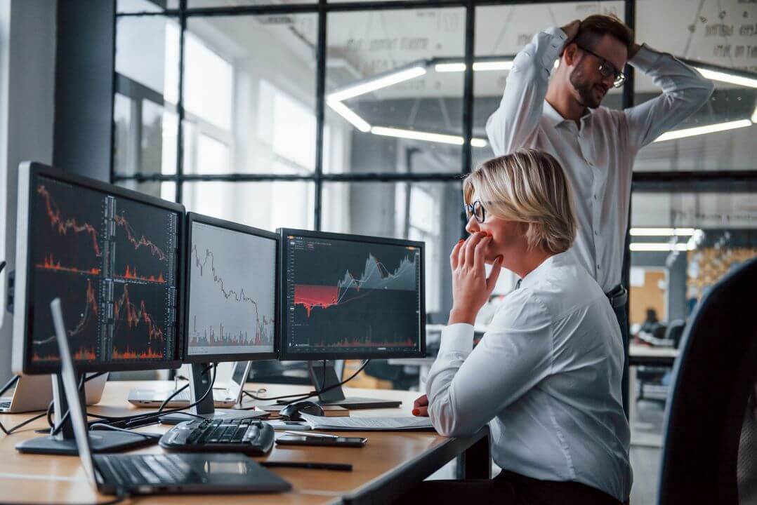 A frustrated woman and man looking at graphs showing a decrease in sales due to stockouts across multiple computer monitors 