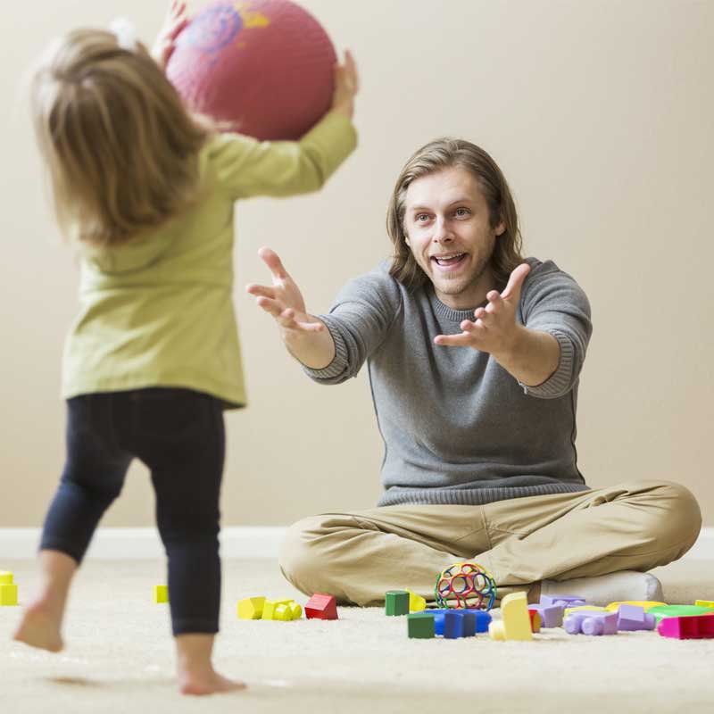 Dad encouraging his daughter to throw him the ball in Floortime therapy