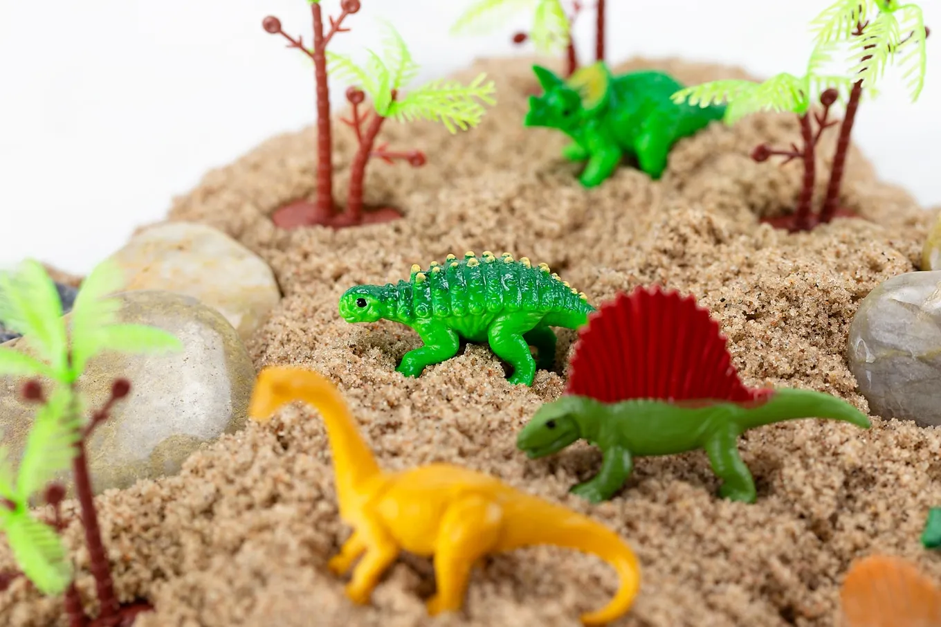 plastic dinosaurs and trees on sand