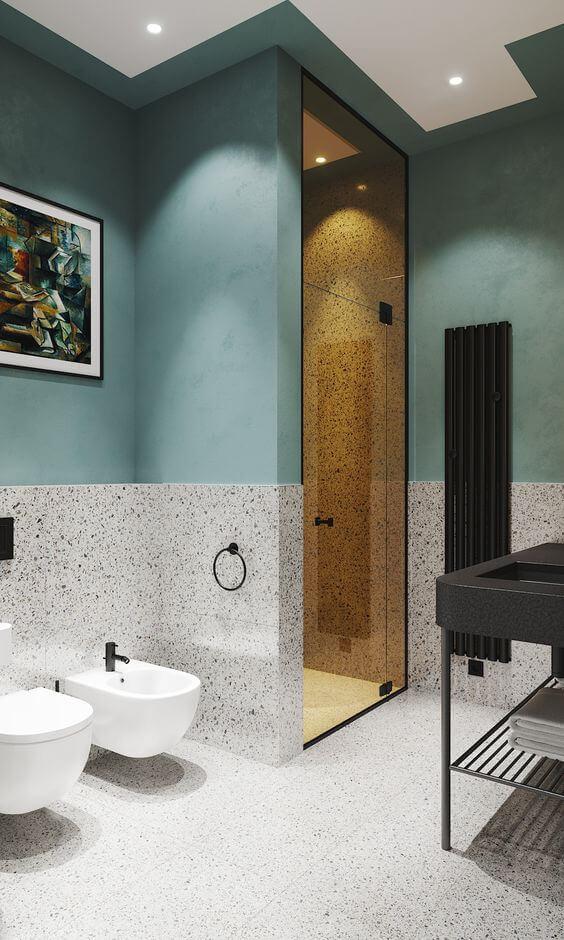 Banheiro com granilite revestindo piso e meia parede, outra metade pintada de azul, louças pretas e porta de vidro para acessar área do chuveiro