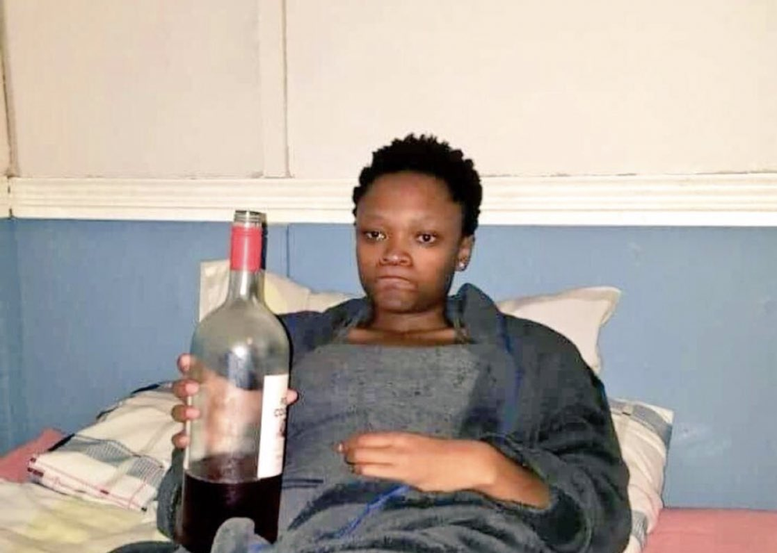 Black female holding a bottle of alcohol dejectedly.