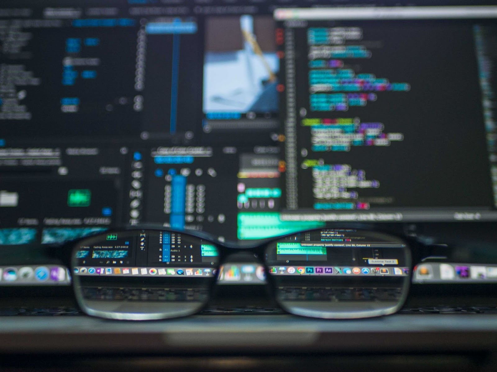 Image of blurred computer screen with focus only shown through a pair of glasses placed on the desk