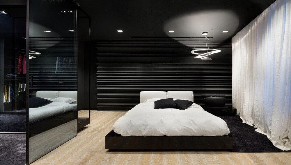 Quarto com cama de casal no chão, piso de madeira, paredes e closet preto.
