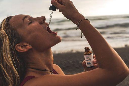 woman using a dropper and holding blooming botanicals cbd oil
