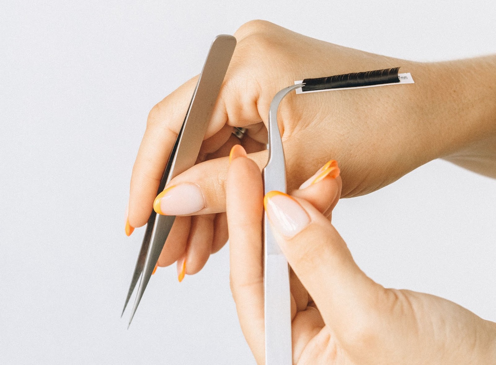 A pair of hands show off tweezers and a strip of eyelashes used for applying eyelash extensions