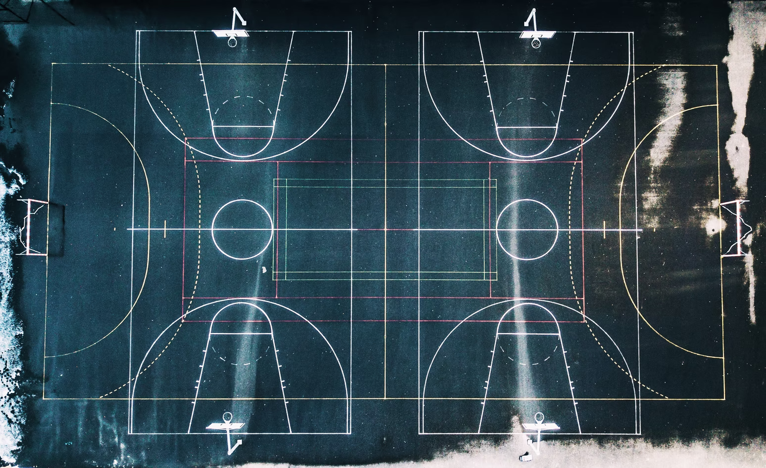 Aerial view of two basketball courts vertically side by side, across a horizontal soccer field.