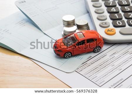 A red toy car, stacks of coins, a calculator, and financial documents on a table
