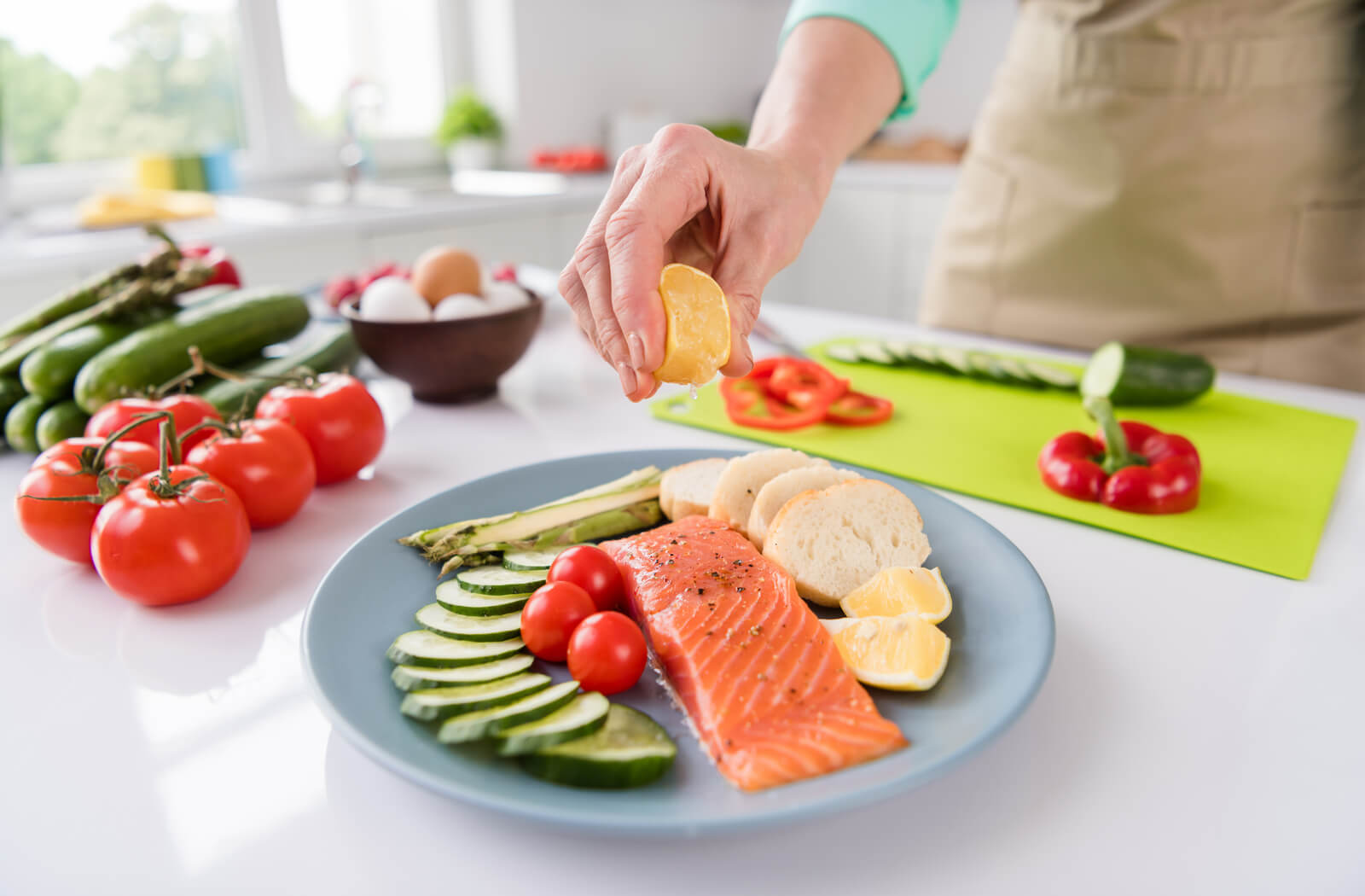a person standing out of frame squeezes half of a lemon over a plat of salmon, zucchini, asparagus, tomatoes and slices of bread
