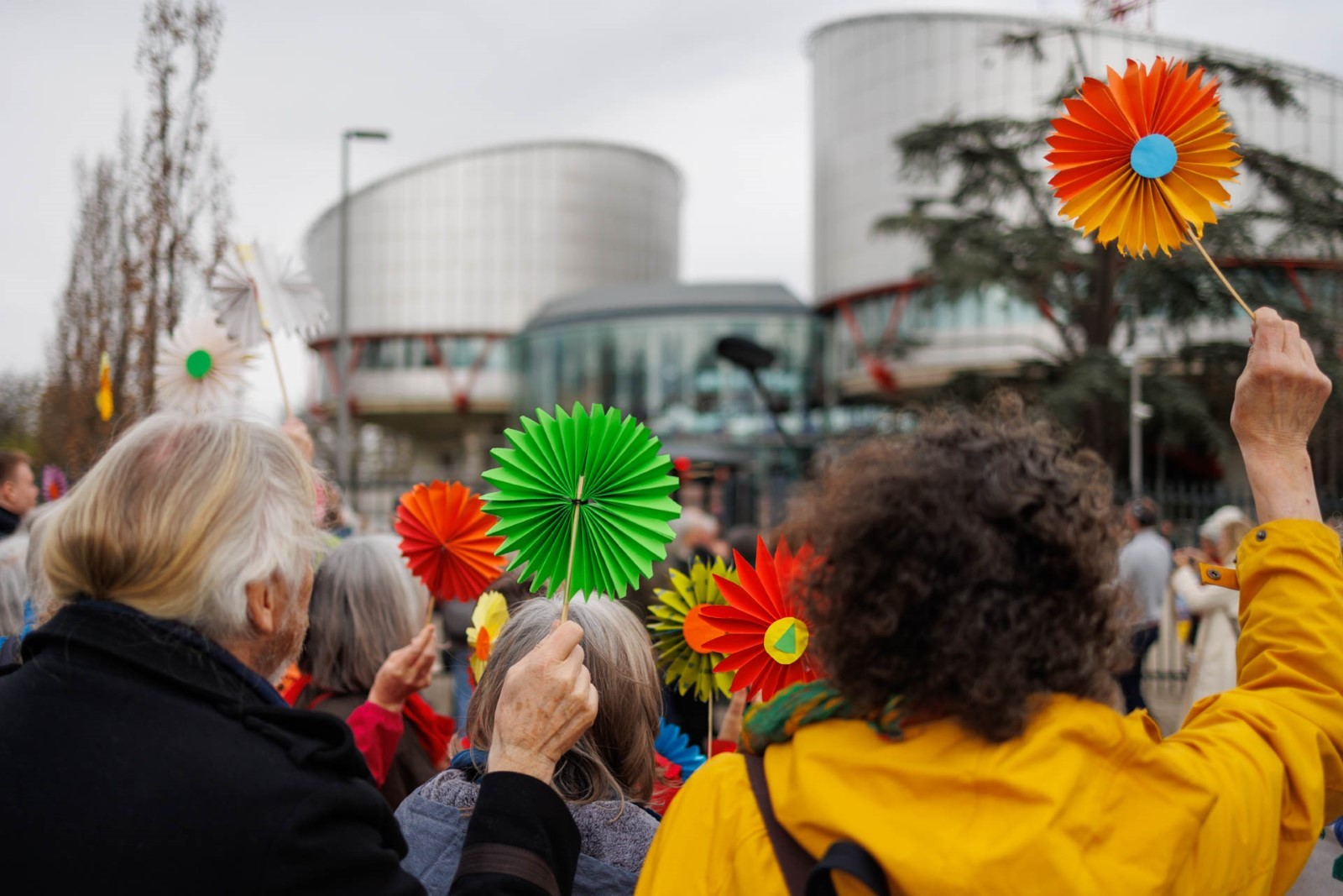 Pensjonister med papirblomster i hånden har møtt opp for å støtte saksøkerne fra Klimaseniorinnen utenfor Den europeiske menneskerettighetsdomstolen i Strasbourg (EMD)