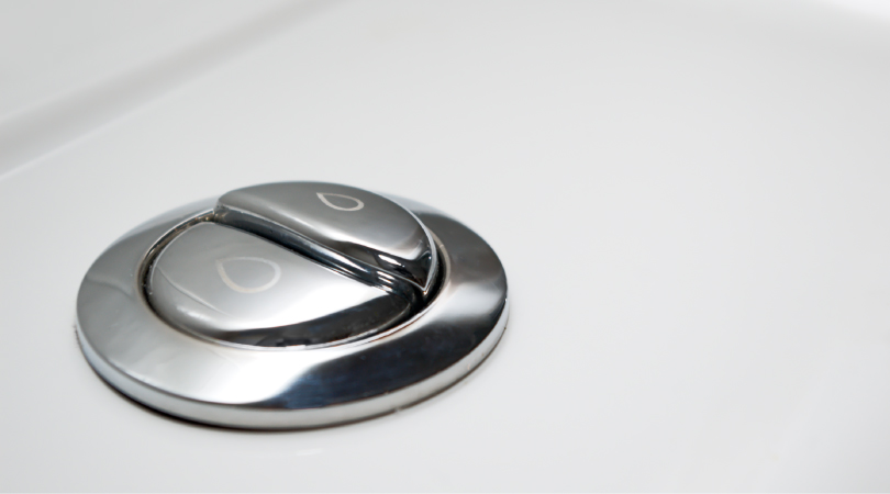 A close-up view of metallic, dual-flush toilet buttons. The left button has a small water drop etched on it, and the right button has a large water drop etched on it.