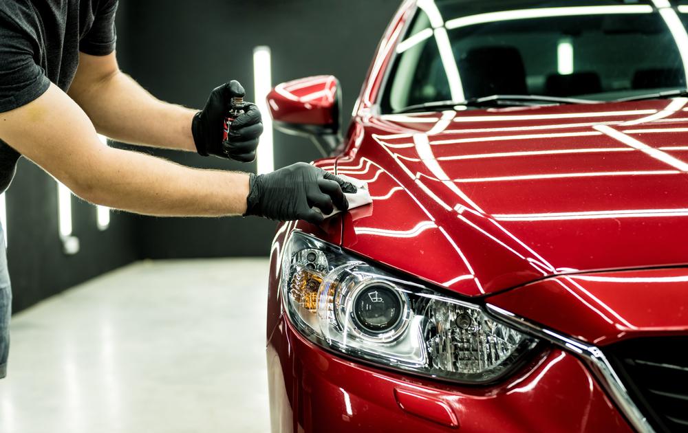 A worker applying ceramic coating to a red car to protect it from environmental damage and enhance its shine.