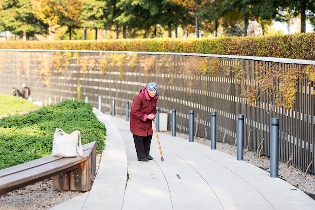 An old lady walks in the park hunched over dressed in a red coat Premium Photo