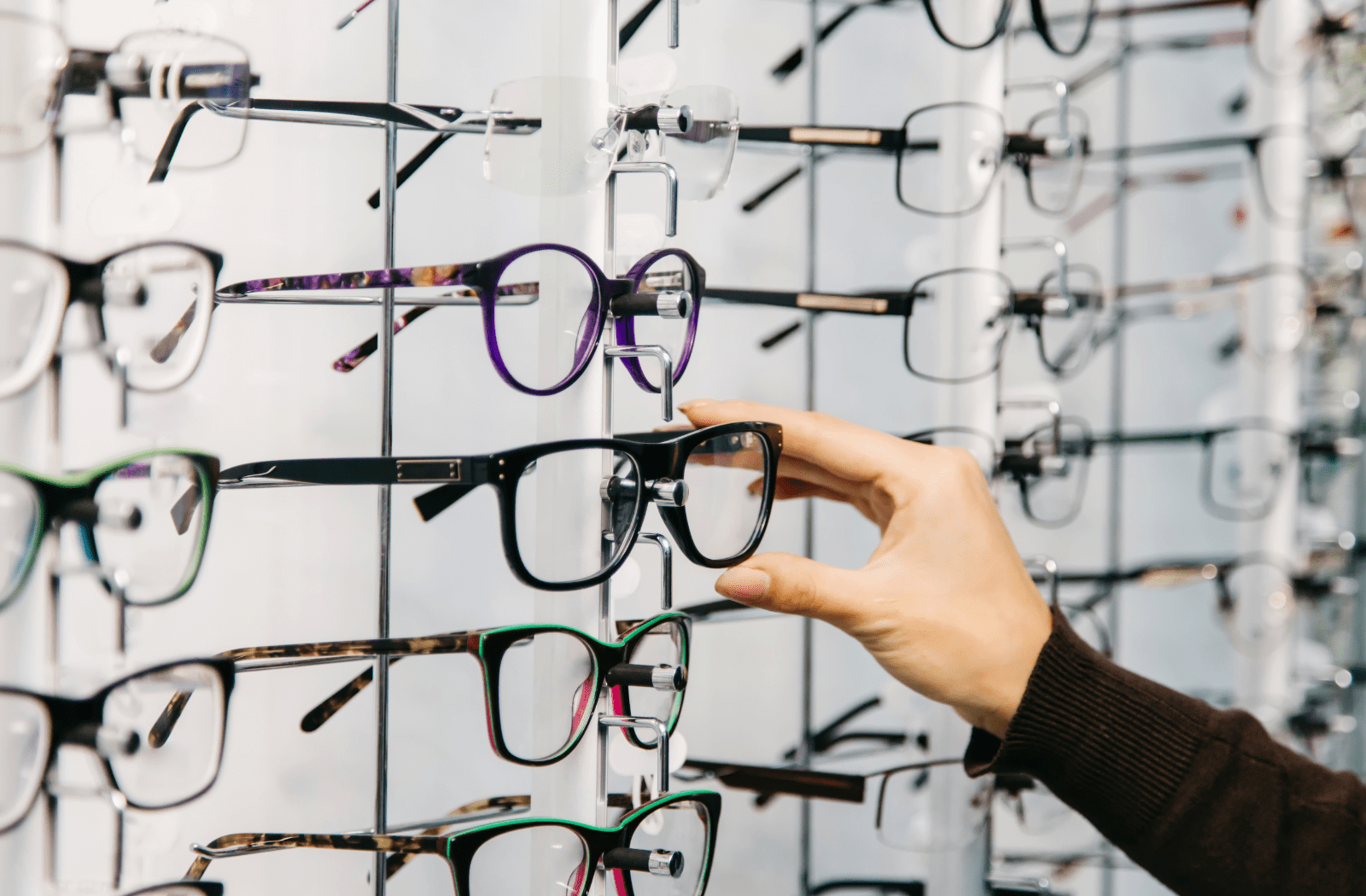 A woman's hand reaching for a pair of prescription glasses for sale to try them on