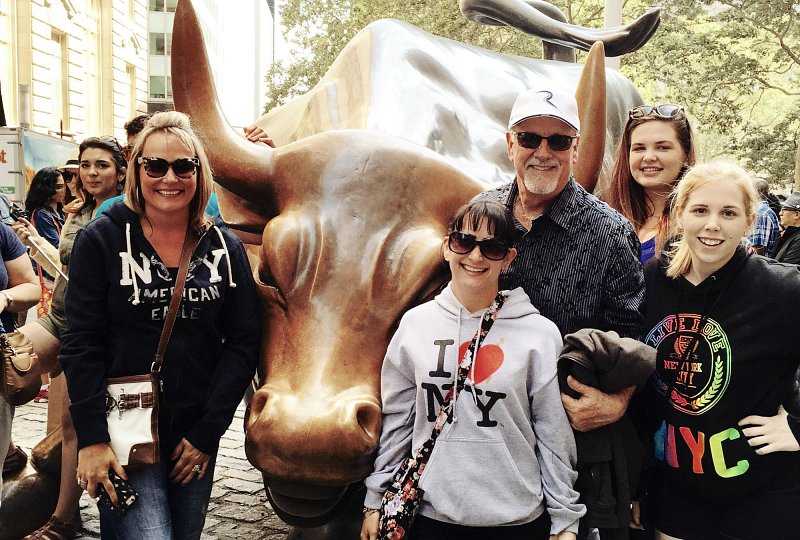padre, madre y tres hijas se paran cerca de la estatua del toro de carga en el distrito financiero