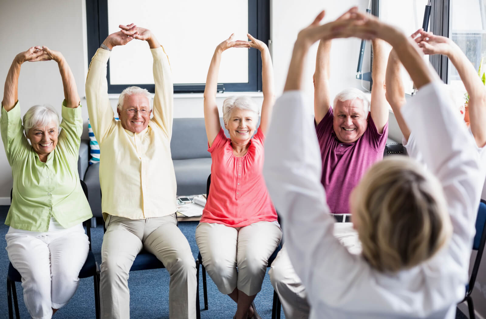 A group of seniors sitting and exercising together under the supervision of trained staff.