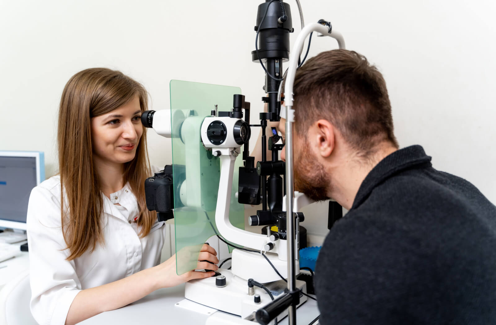 A female optometrist examining the eyes of a young man using a medical device to detect potential eye problems.
