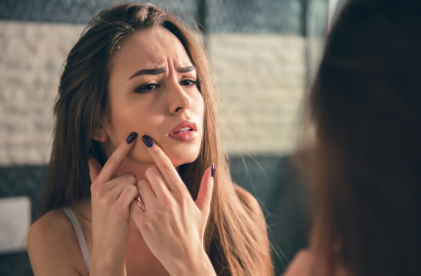 brunette woman looking in the mirror and popping a zit
