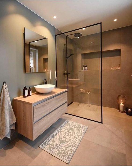 Banheiro com paredes cinza, piso em tom neutro antigo, armário de madeira, box de vidro com moldura preta, torneira e chuveiro pretos.