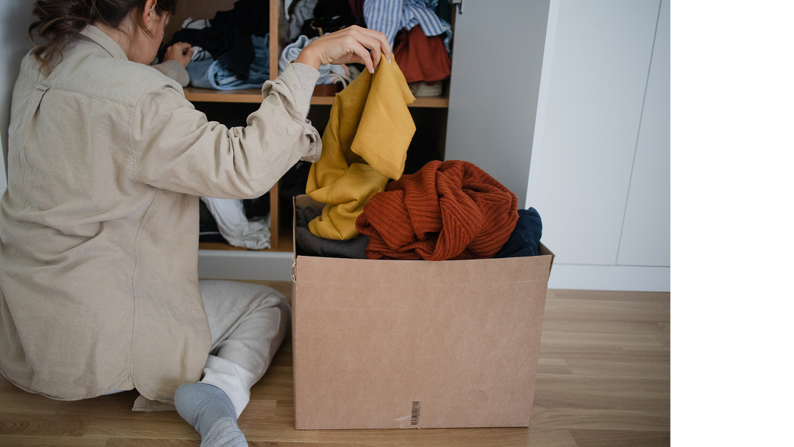 a woman seating on the floor while putting clothes inside a box