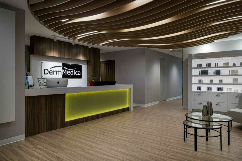 The front reception area and desk of DermMedica, a skincare clinic near The Shore; the desk is lit with a green backlight, which contrasts with the black and white sign and modern wood accent interior design