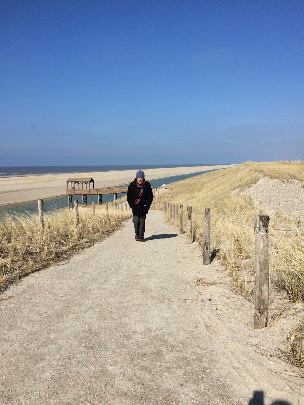 man in black jacket walking on gray sand during daytime