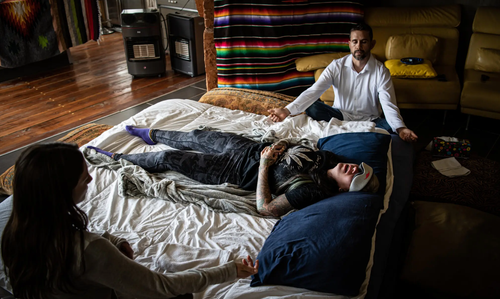 Mulher deitada na cama, em sessão de psicoterapia assistida por psicodélica, com dois terapeutas dando suporte