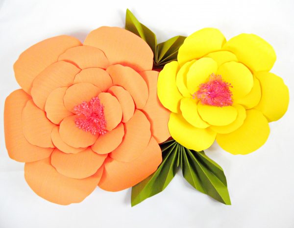 Two finished orange and yellow giant hibiscus paper flowers are adorned with green paper leaves. 