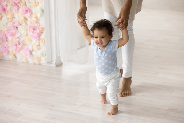 baby holding hands with an adult, adult's face is not seen. baby holds both of the adults hands facing forward, in an attempt to lean how to walk. 