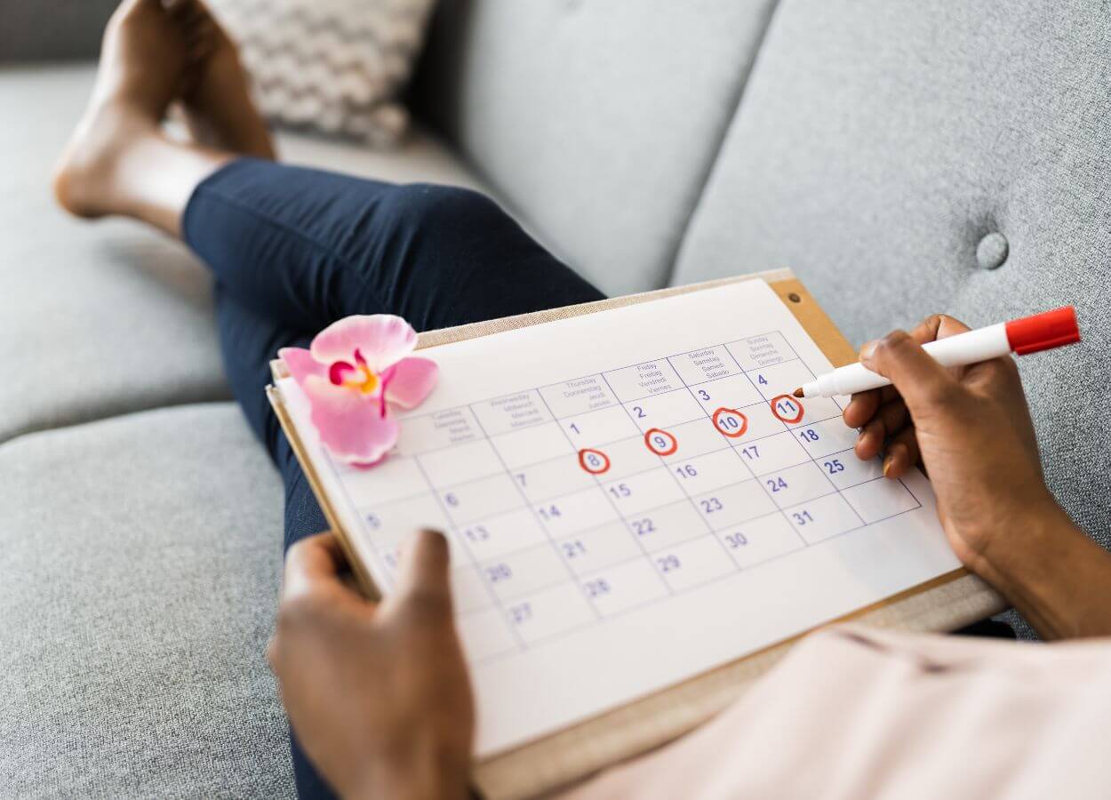 Woman sitting on a couch tracking her period using a calendar