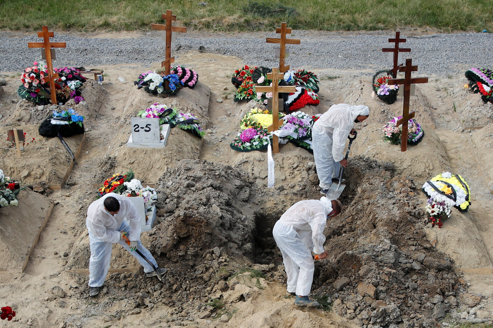 Workers in hazmat suits burying bodies in graves due to the pandemic. 