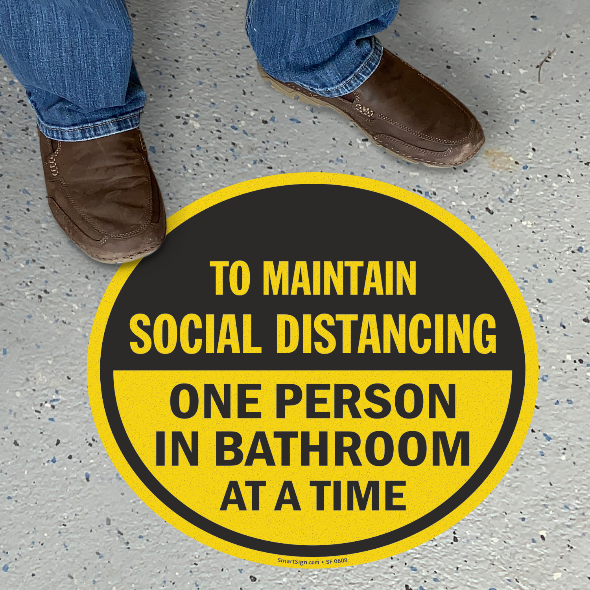 Circle sign on the floor indicating one person is allowed in the bathroom at a time to maintain social distancing.