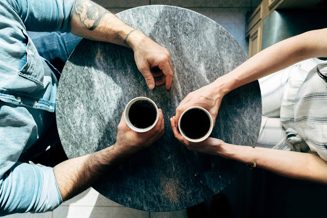 Two people holding cups of coffee while seated opposite to each other at a round table