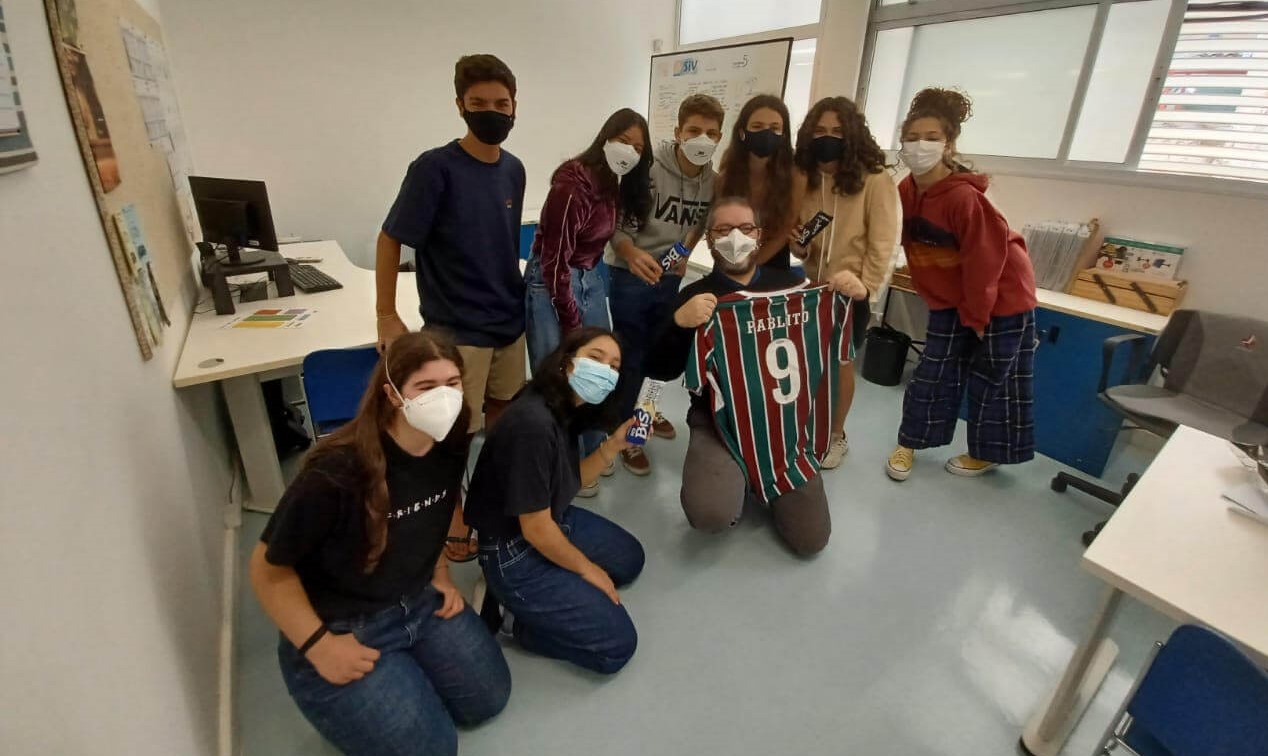 A imagem mostra um grupo de alunos e alunas com um professor.