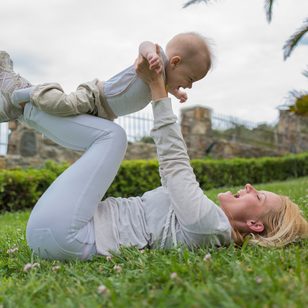 Mother lying on the grass and playing with her baby outside the house