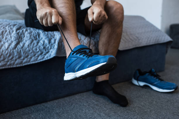 man tying sneaker laces Cropped shot of man sitting on bed and tying laces on jogging sneakers mens shoes stock pictures, royalty-free photos & images