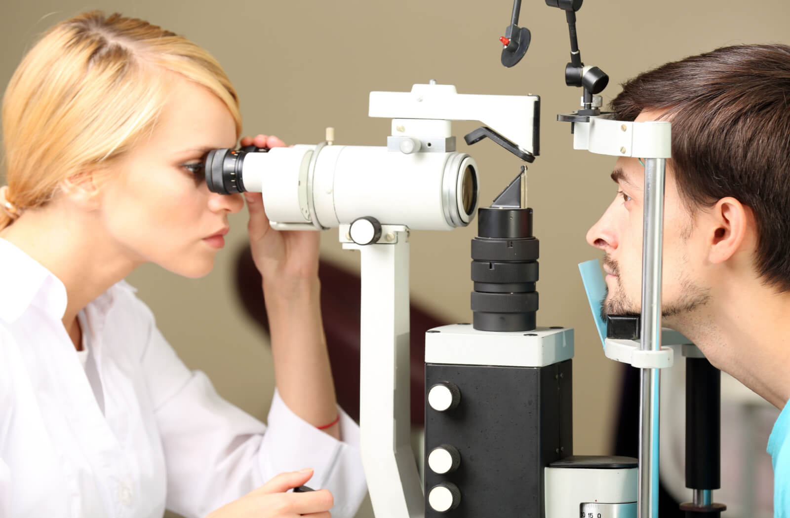 A female optometrist examining the eyes of a man using a medical device to detect potential eye problems.