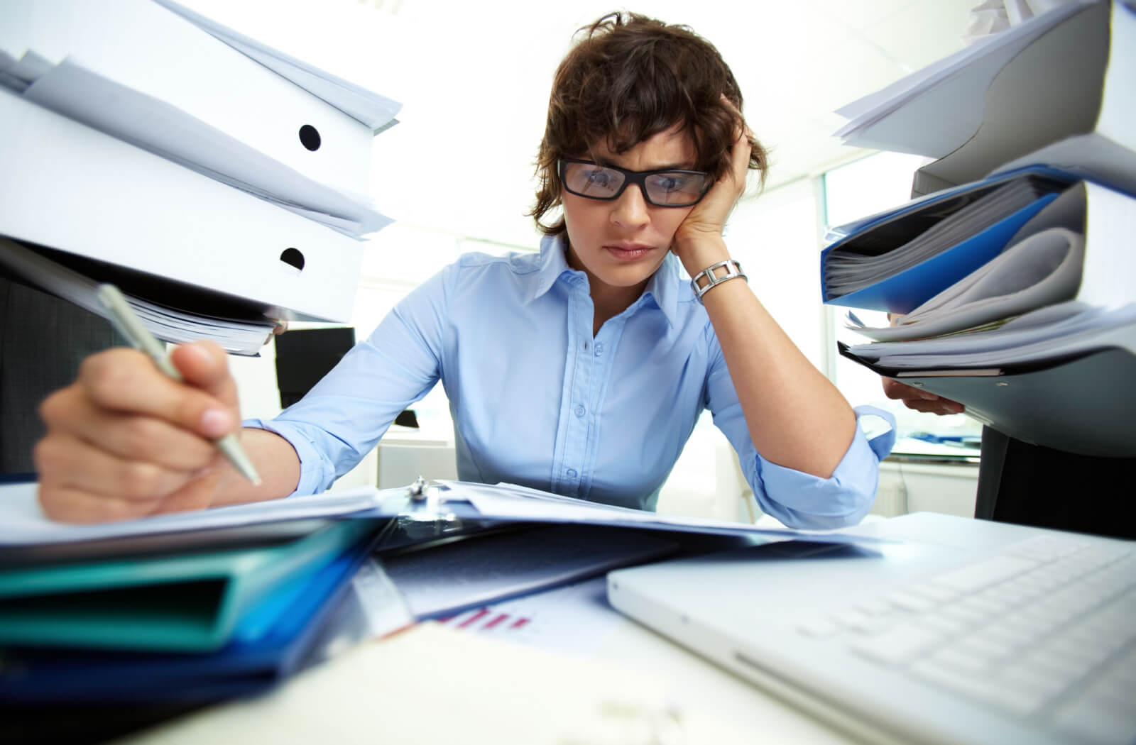 A professional-looking woman stressed by the amount of paperwork on her desk.