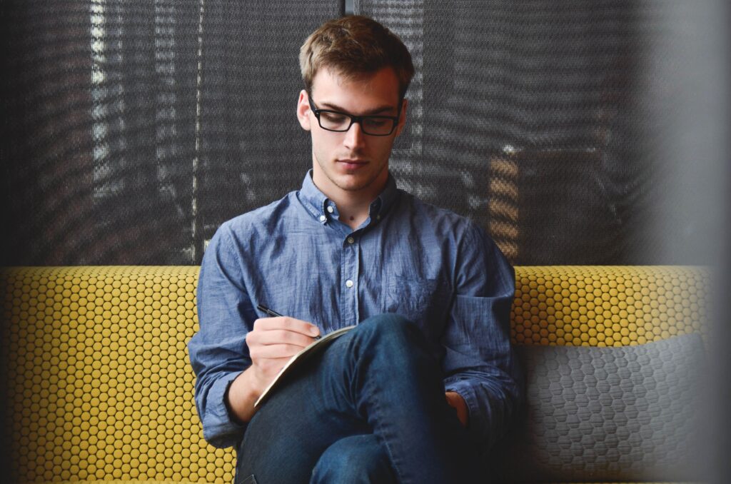 A man sits cross legged on a sofa with a notepad, asking who am i about his identity