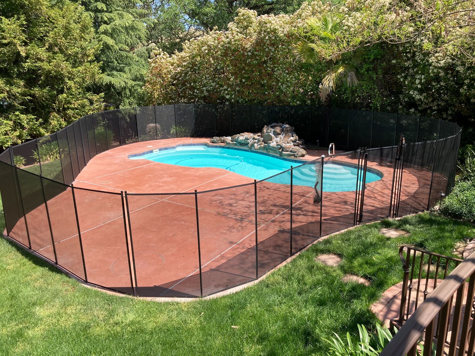 Black mesh swimming pool fence installed around a backyard pool